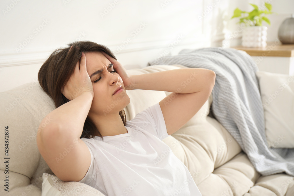 Young woman suffering from migraine on sofa at home Young woman suffering from migraine on sofa at home
