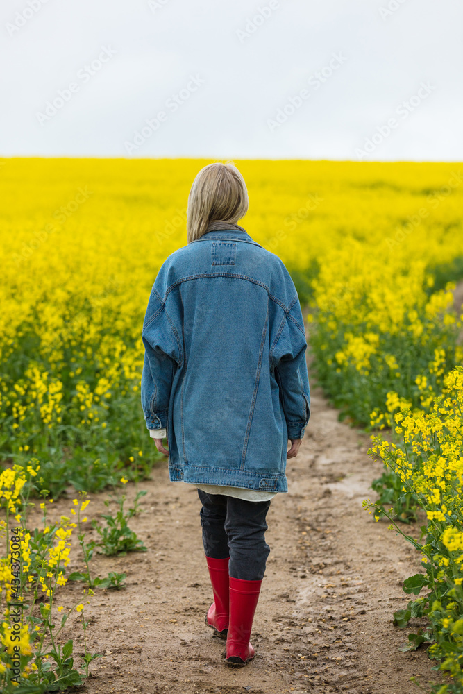 Beautiful blonde in denim jacket and wellington boot on yellow rapeseed field