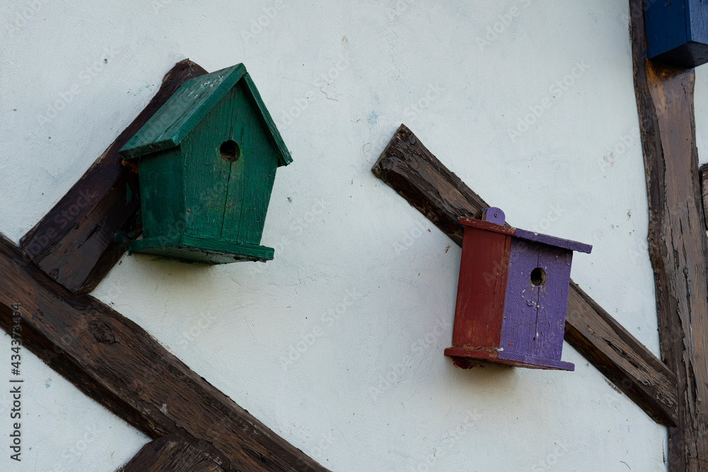 Bright birdhouses attached to a decorative tree against the backdrop of the wall of the house.