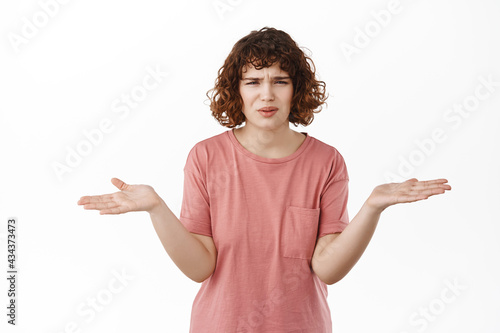 Whats wrong, wtf going on. Confused and annoyed young woman spread hands sideways, grimacing and staring questioned, cant understand something strange, standing over white background