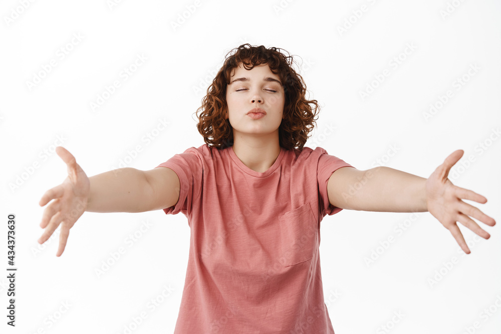 Cute romantic girl close eyes, pucker lips for kiss and spread hands sidways, hugging and kissing someone dear, standing against white background in warm embraces Cute romantic girl close eyes, pucker lips for kiss and spread hands sidways, hugging and kissing someone dear, standing against white background in warm embraces