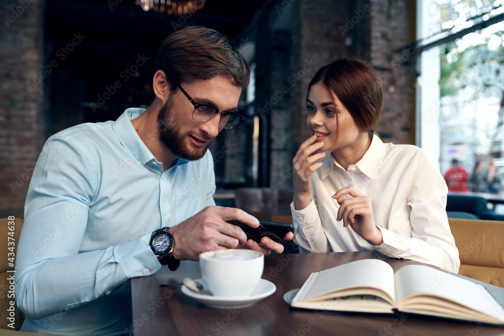 Cheerful man and woman are sitting in a cafe at the table working communication technology Cheerful man and woman are sitting in a cafe at the table working communication technology