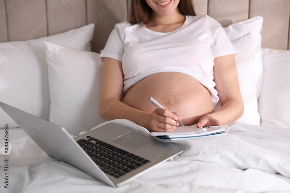 Fototapeta premium Pregnant woman working on bed at home, closeup. Maternity leave