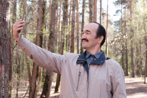 Senior Asian man using mobile phone for taking selfies in forest park.