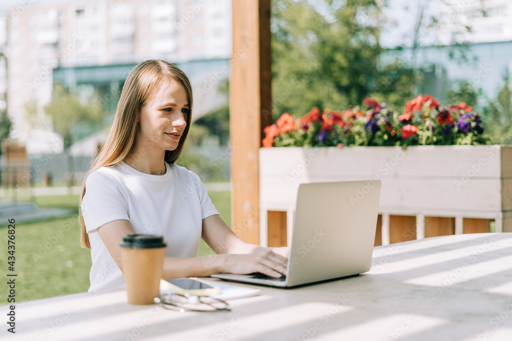 Beautiful blonde business woman working at laptop sit down on bench outside in public park. Happy student lady girl in white t-shirt distance learning, education and online shopping. Beautiful blonde business woman working at laptop sit down on bench outside in public park. Happy student lady girl in white t-shirt distance learning, education and online shopping.