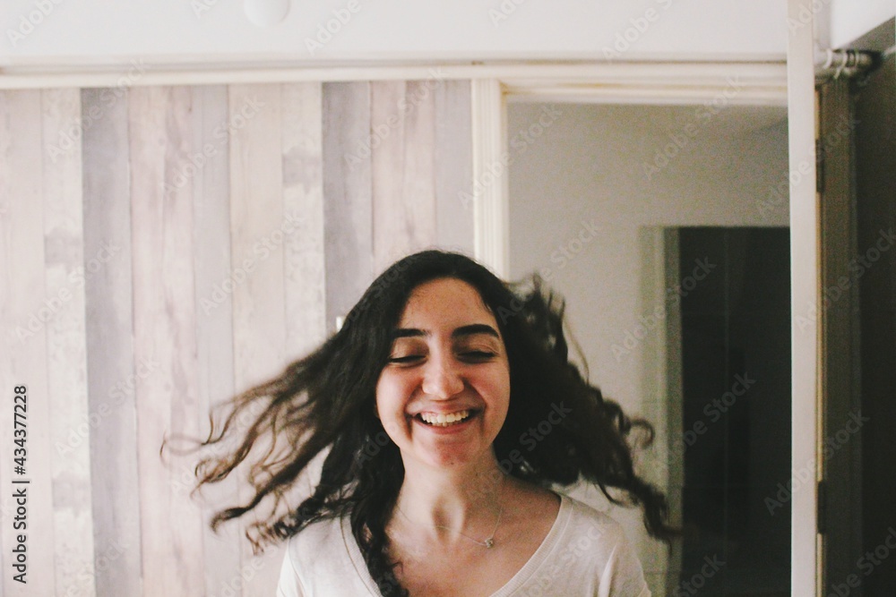 Portrait of happy smiling young woman with long hair in fast motion indoors at home 