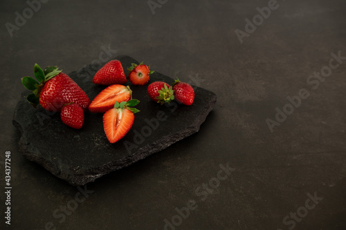 Ripe juicy red beautiful strawberry close-up is an appetizing fresh snack on a granite slab plate