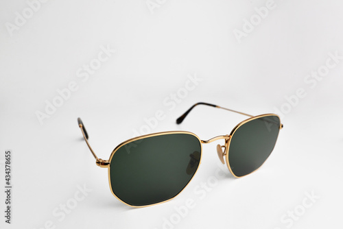 Men accessories, closeup sunglasses with gold frame. Square sunglasses with round bottom, black clear lenses and thin golden wrap around frames isolated on white background.