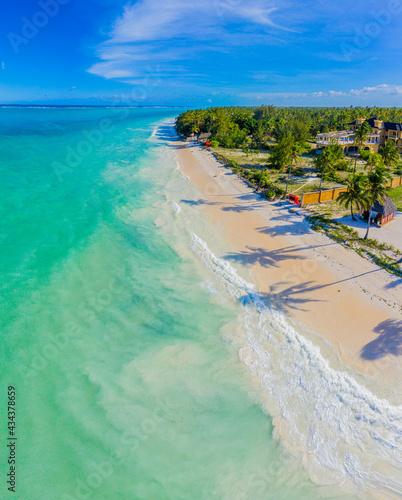 Fototapeta Naklejka Na Ścianę i Meble -  Aerial view of palms on the sandy beach of Indian Ocean at sunny day. Summer holiday in Zanzibar, Africa. Tropical landscape with palm trees, white sand, blue water, hotels. Top view of sea coast