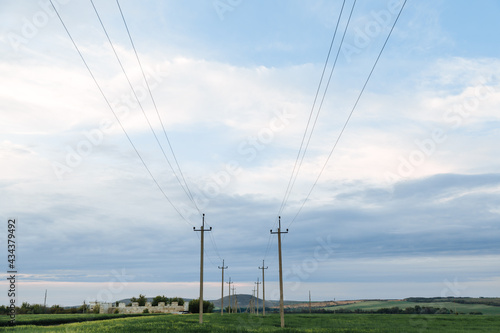 High voltage lines and power pylons in a green agricultural landscape and cloudysky on sunset time background