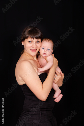 Love of a mother and baby. Family. Smiling baby and his mom. Young mother holding her newborn child in hands. Caucasian mom holding her cute infant on the black background. Newborn baby with mommy