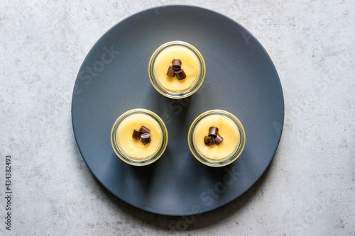 Three glasses with vanilla pudding triangularly arranged on a blue plate shoot from directly above photo