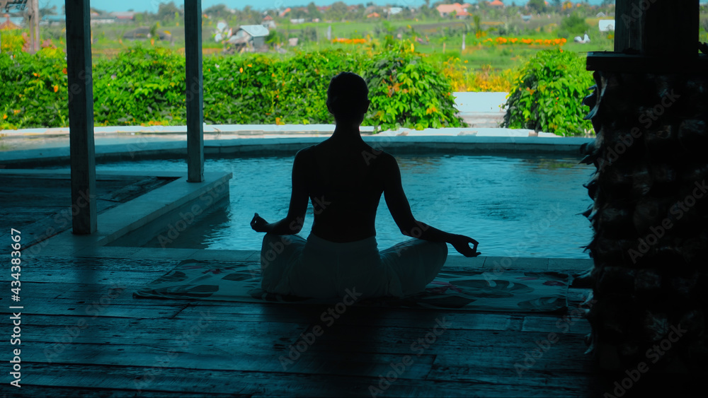 European brunette girl sits on a towel and yoga in a lounge room overlooking green fields European brunette girl sits on a towel and yoga in a lounge room overlooking green fields