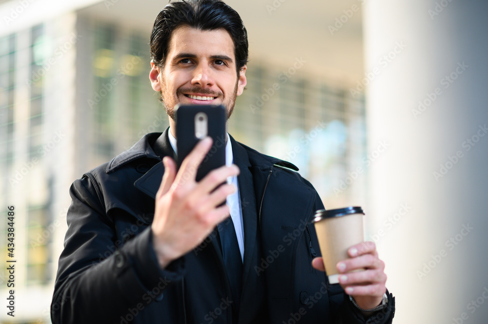 Handsome elegant dressed man using his smartphone and holding a cup of coffee Handsome elegant dressed man using his smartphone and holding a cup of coffee