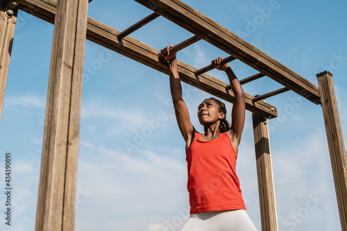 African young woman climbing monkey bars in military training boot camp outdoors at city park - Focus on girl face photo