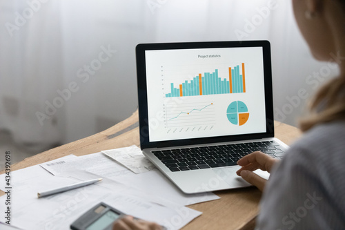 Analyzing data. Close up over shoulder view of young businesswoman preparing financial report managing project statistics counting in laptop business application. Focus on charts graphs on pc screen photo