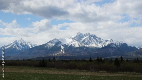 Timelapse of clouds over landscape under High Tatras rocky mountains in spring season, Slovakia. Green meadows in contrast with mountains covered with snow.