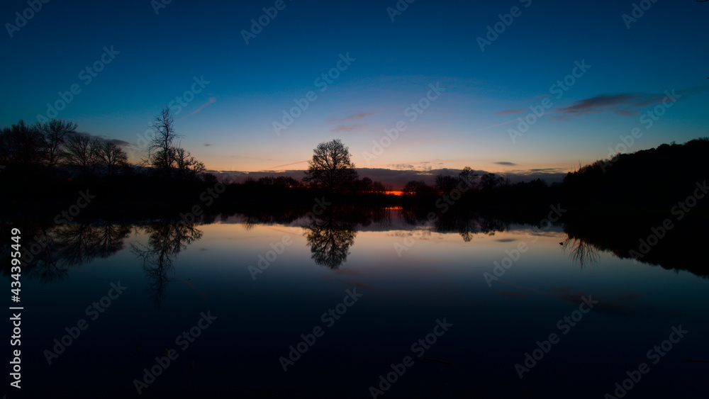 Fototapeta premium Lever de soleil et son reflet sur de l'eau des marais de Bazouges cré sur Loir avec silhouette d'arbres en fond
