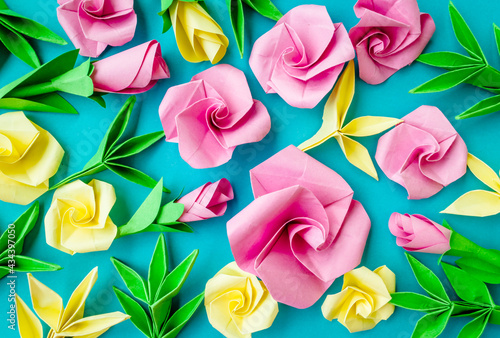 Origami paper background with flowers and leaves. Handmade pink roses backdrop. Origami composition. Paper craft.