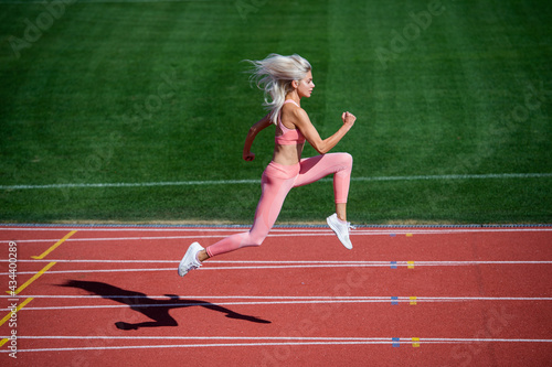 athletic woman in fitness wear running on stadium, endurance