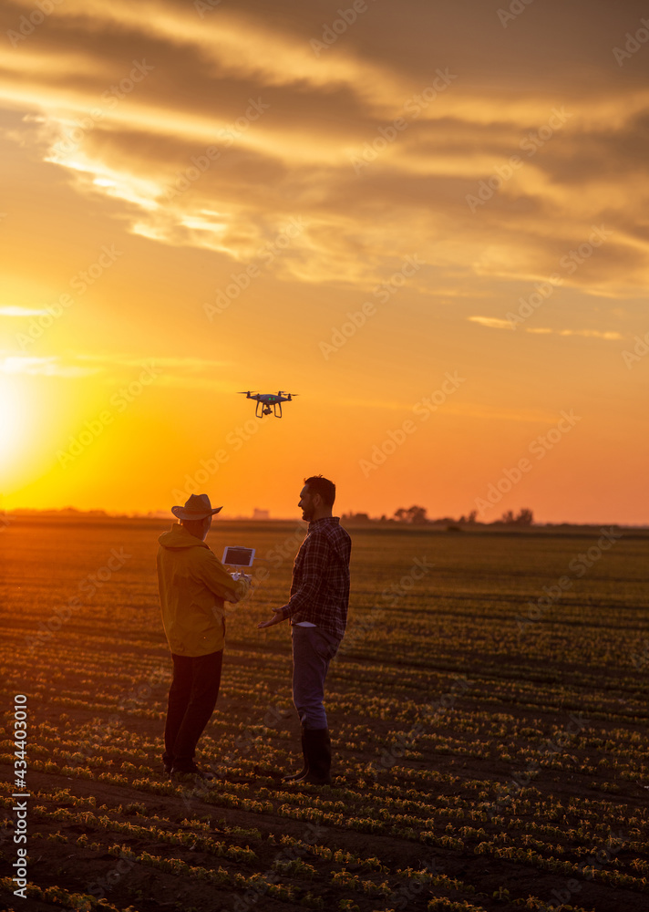 Two satisfied farmers standing in field using drone