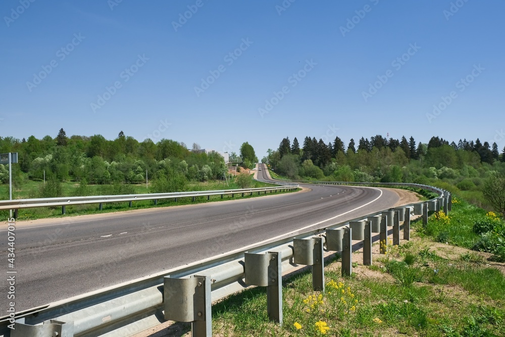 Empty asphalt rural road winding across farmland and forest in countryside. Road background. Empty asphalt rural road winding across farmland and forest in countryside. Road background.