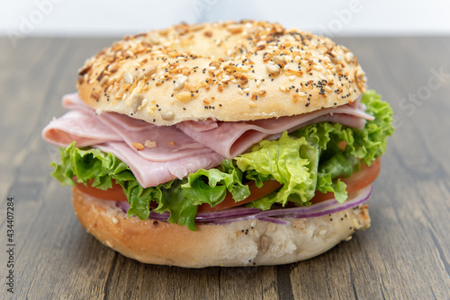 Everything bagel bun envelops this non traditional ham sandwich loaded with lettuce, meat slices, and onion.