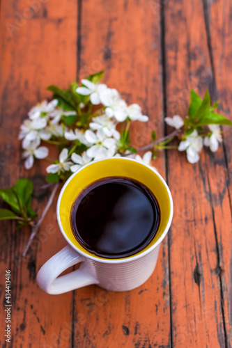 a cup of coffee on a dark, worn rustic wooden table. The composition is decorated with a twig with white flowers. Cherry tree flowers. Selective focus.