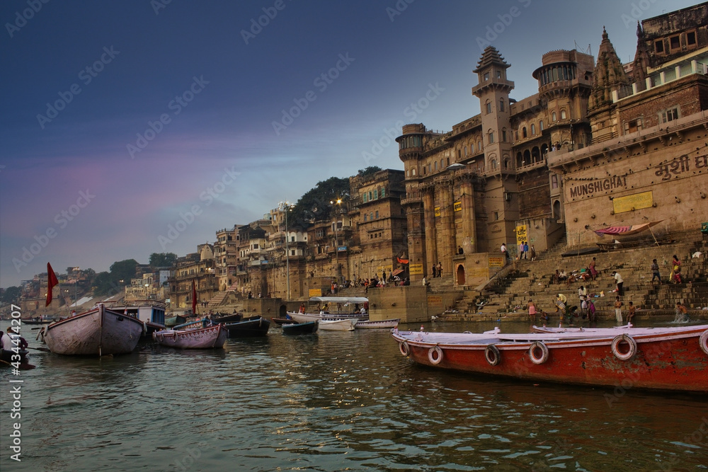 Varanasi, India: People and tourists on wooden boat sightseeing in Ganges river near Munshi ghat against ancient city architecture as viewed from a boat during morning time