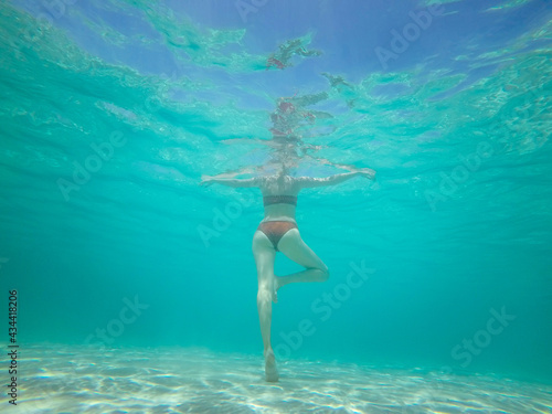 Rear underwater view of women body swimming under turquoise water in the sea.