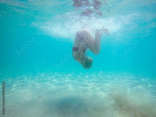 Under water photo of a woman in bikini diving in turquoise sea water.