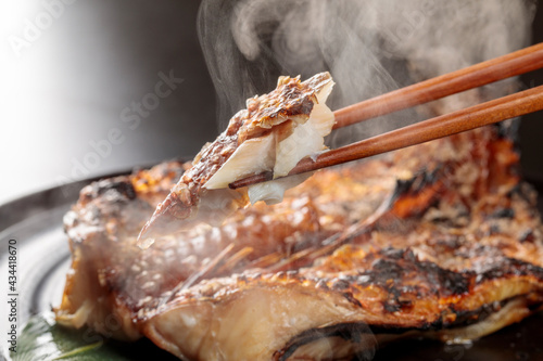 ゆげが上がる焼きたての魚を箸で摘むシーン