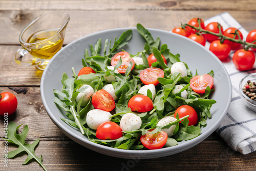 Diet and healthy salad with arugula, cherry tomatoes, mozzarella cheese and olive oil on wooden table background. Mediterranean cuisine. Close up