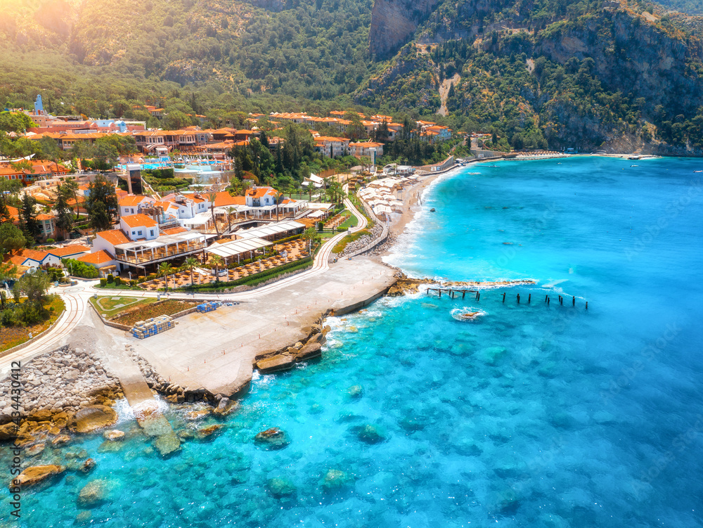 Aerial view of beautiful hotel and blue sea at sunny day in summer in Oludeniz, Turkey. Top view of buildings, clear water, stones, beach, green palm trees, mountain. Luxury resort. Tropical landscape