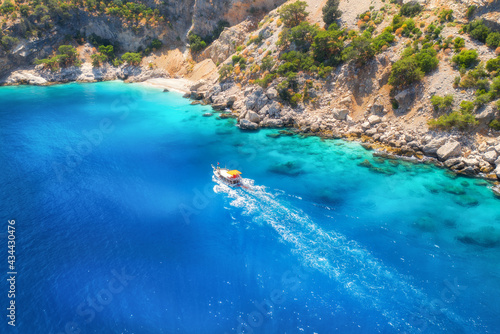 Speed boat in blue sea at sunrise in summer. Aerial view of floating motorboat in sea bay. Tropical landscape with yacht  clear water  rocks   stones  mountain  green trees. Top view. Oludeniz  Turkey
