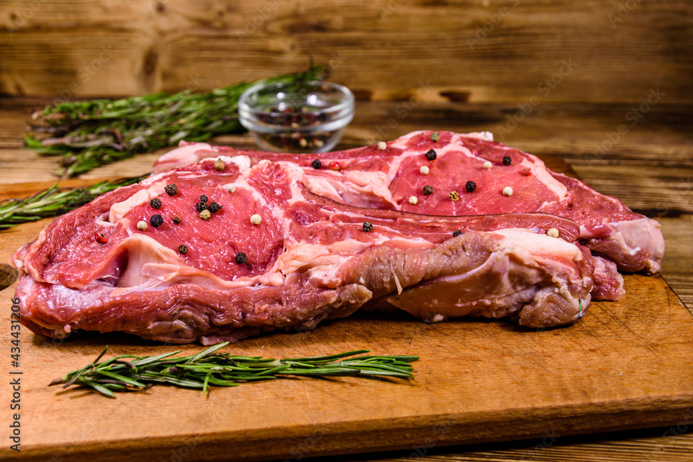 Raw ribeye steak, glass jar with spices and rosemary on cutting board