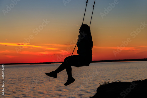 Silhouette of a girl on rope swing above river at sunset