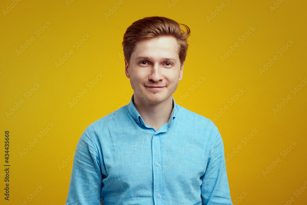 Young man wears blue shirt and poses in studio against yellow background Young man wears blue shirt and poses in studio against yellow background