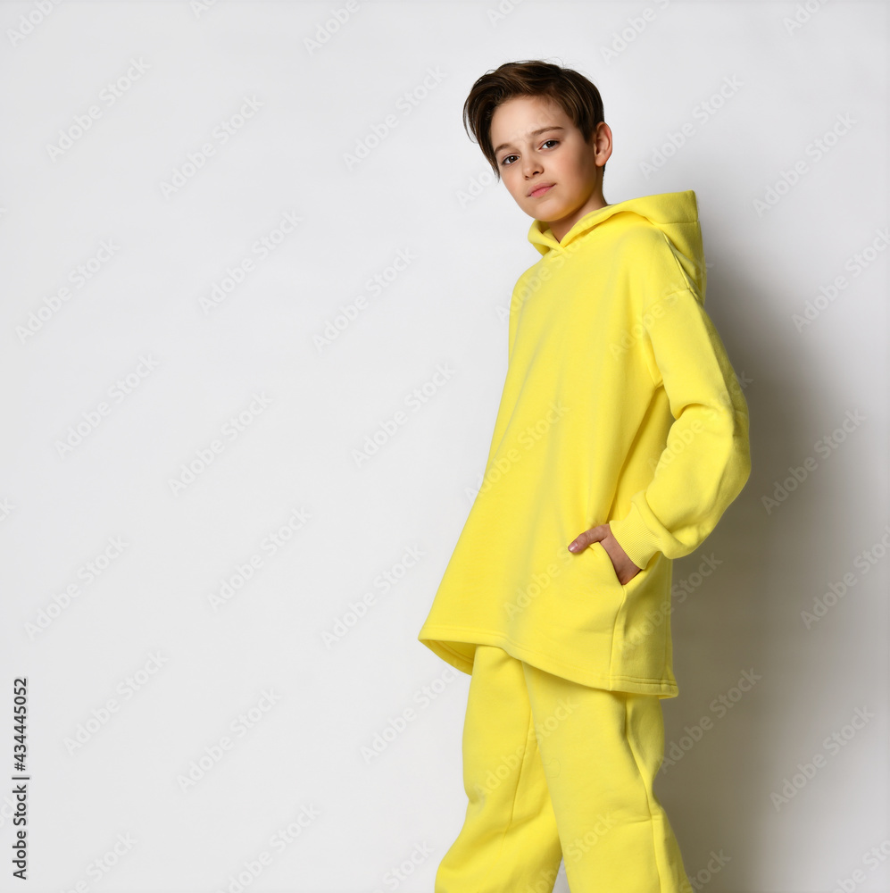 teenage boy wearing a bright yellow tracksuit. Stylish cool teenager stands with hands in pockets, stands on a white background. Children's sports fashion concept. teenage boy wearing a bright yellow tracksuit. Stylish cool teenager stands with hands in pockets, stands on a white background. Children's sports fashion concept.