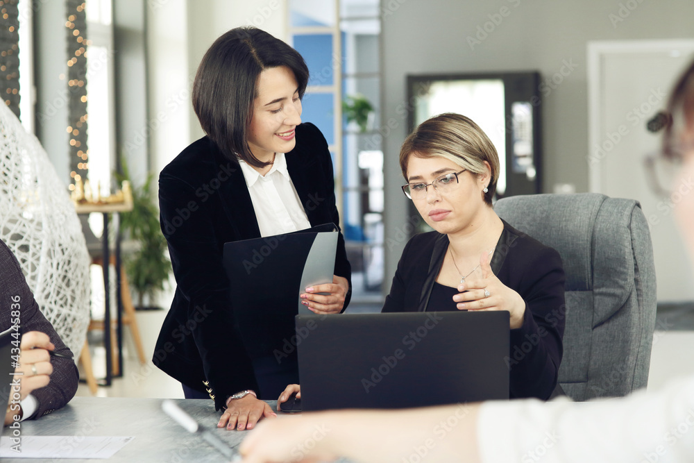 Two young business women in the office, analyzing information looking into a laptop and smiling Two young business women in the office, analyzing information looking into a laptop and smiling