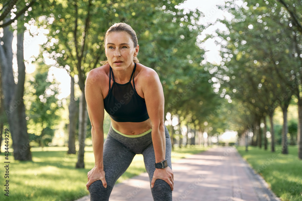 Rest for a while. Beautiful sporty woman in sportswear taking a break while jogging in a green park on a sunny summer day Rest for a while. Beautiful sporty woman in sportswear taking a break while jogging in a green park on a sunny summer day