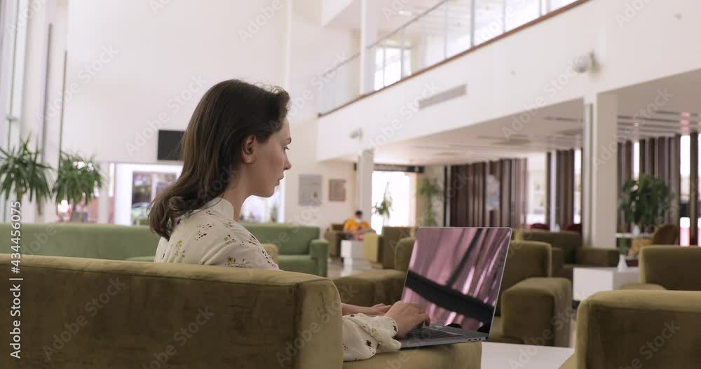 Focused freelancer working on laptop computer while sitting on hotel lobby bar. Women working remotely on a business trip. Focused freelancer working on laptop computer while sitting on hotel lobby bar. Women working remotely on a business trip.