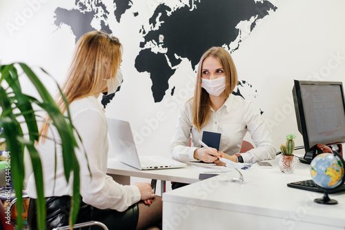 Travel agent having a client in light modern office of tour agency, choose destination. Assistant speaking in face mask in the travel agency to clients. protection during covid pandemic  photo