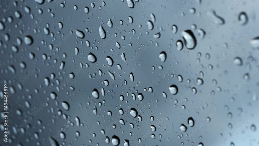 Water raindrop on a clear window glass. Raining on a car windscreen on a moody day. Moving droplets close up in front of a dark cloudy sky. Liquid fluid splashing on the windshield. Water raindrop on a clear window glass. Raining on a car windscreen on a moody day. Moving droplets close up in front of a dark cloudy sky. Liquid fluid splashing on the windshield.