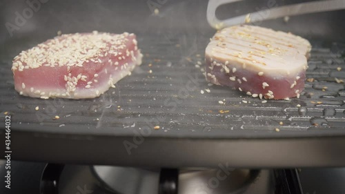 Flipping a steak of yellowfin tuna on a grilling pan in 4K. Concept turning on the other side and frying and cooking tuna steak in slow motion.