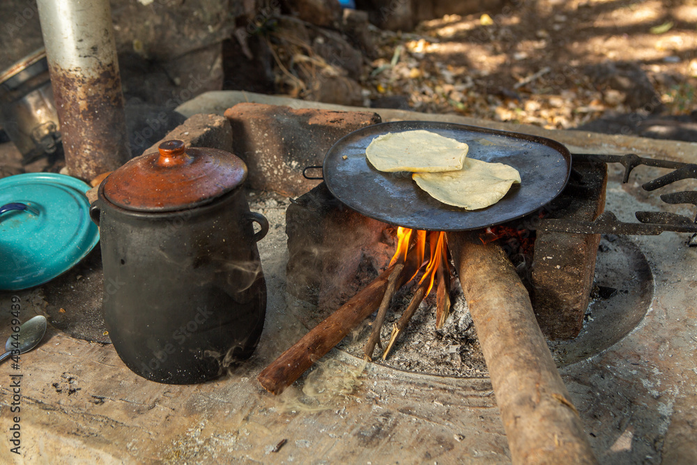 Tortillas en comal de fuego de leña junto a olla de barro con