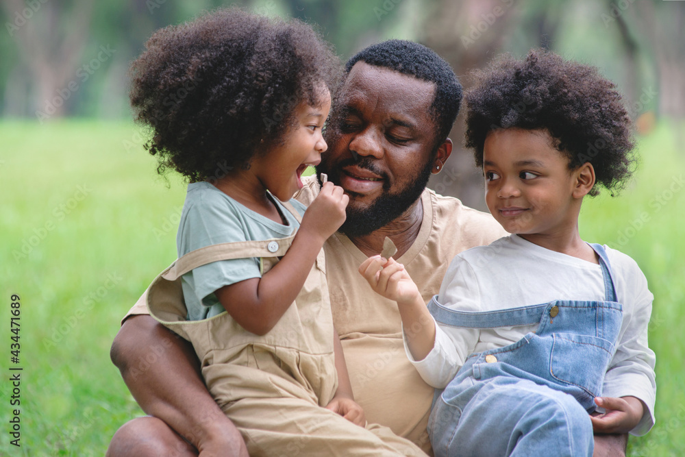African father and daughter and son had a great time at the outdoor park, two children happily sitting on their father's lap, Father's day African father and daughter and son had a great time at the outdoor park, two children happily sitting on their father's lap, Father's day