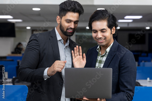 Fotografie Portrait of two young handsome Indian businessmen looking into phone, discussing project, corporate environment
