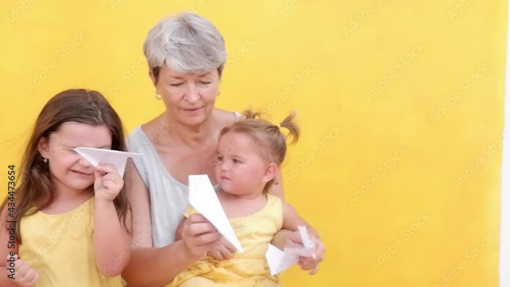 Grandmother with granddaughters playing with paper planes on yellow background Grandmother with granddaughters playing with paper planes on yellow background