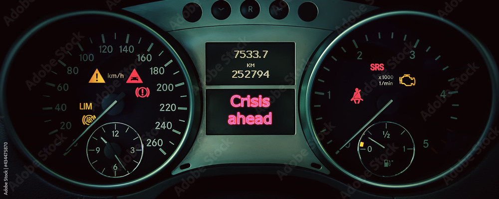 CRISIS AHEAD is written on the dashboard of the car next to the controls and mileage indicators.